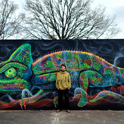 L'artiste situé à côté d'un caméléon crée des graffitis colorés en vert, bleu et rose.
